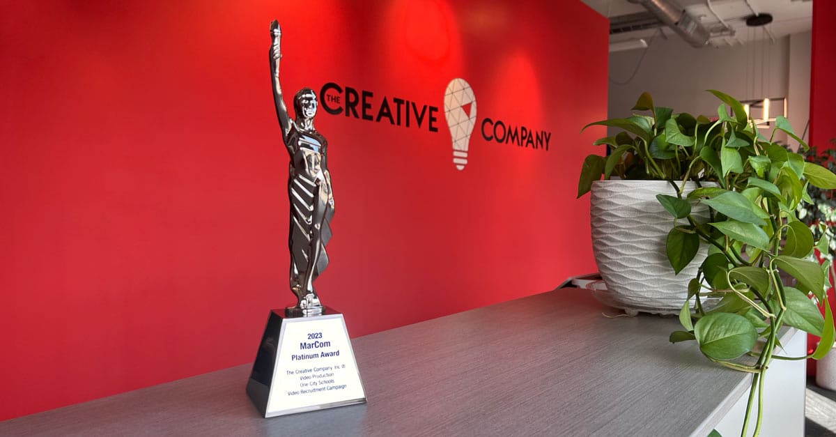 Photo of the Platinum MarCom award The Creative Company won in front of the office's red wall with the company logo graphic.