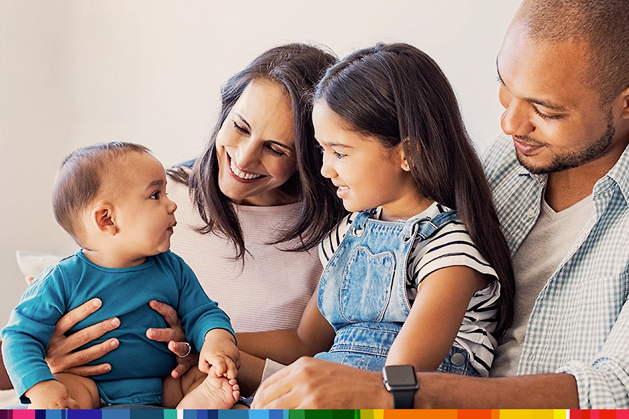 Smiling family sitting together with parents, young daughter, and baby, enjoying a warm moment at home